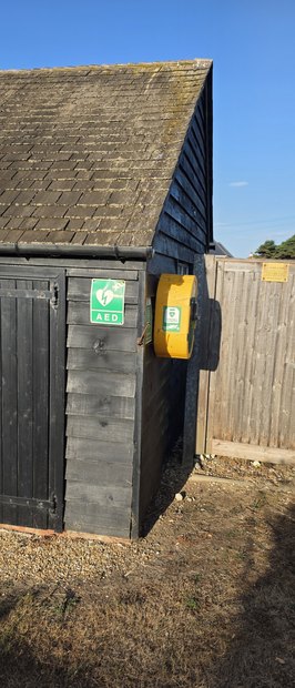 The yellow defibrillator cabinet on the end wall of the beach huts